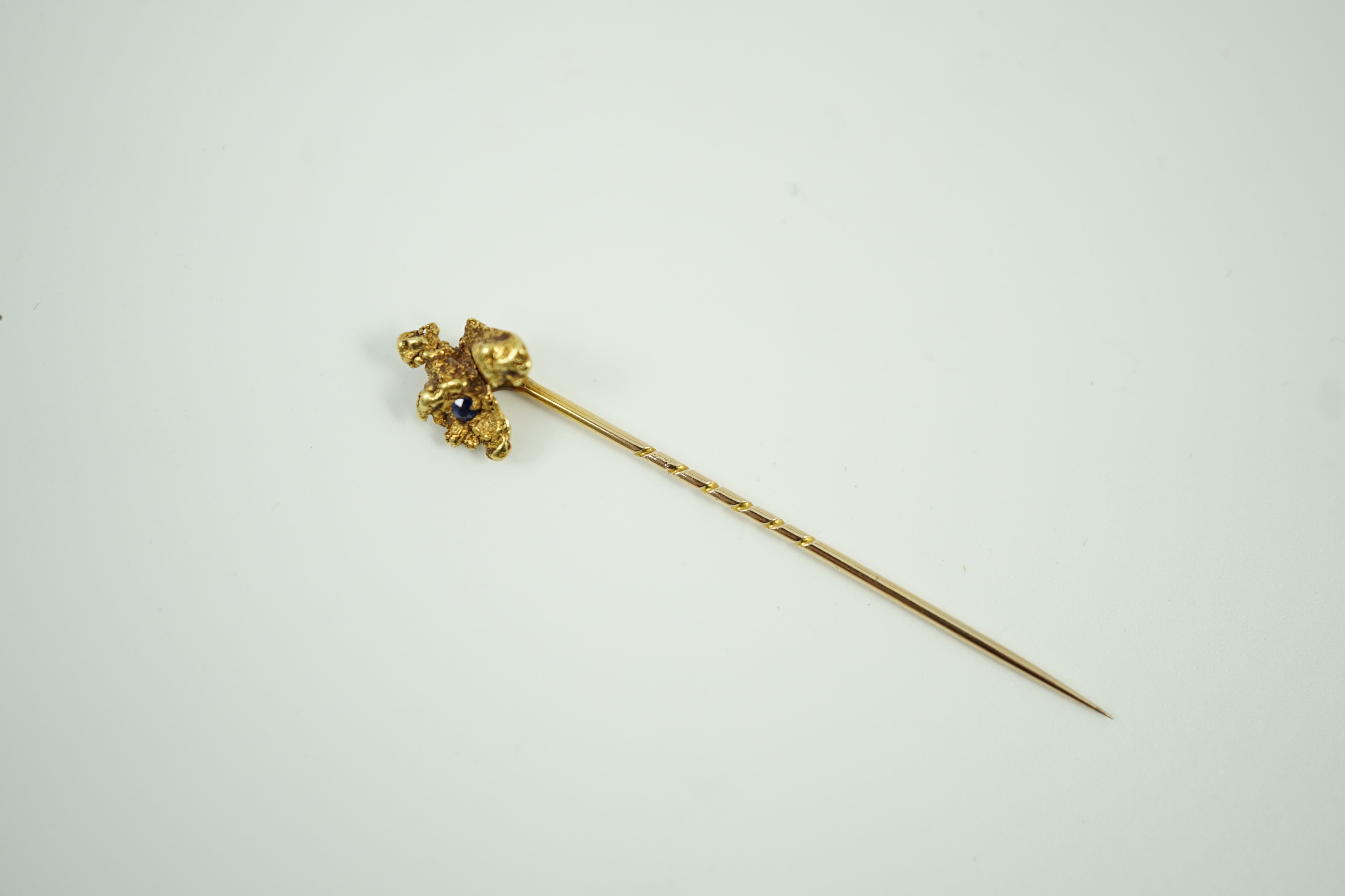 A late Victorian yellow metal and single stone sapphire set 'nugget' stick pin, 62mm, gross weight 3.2 grams.